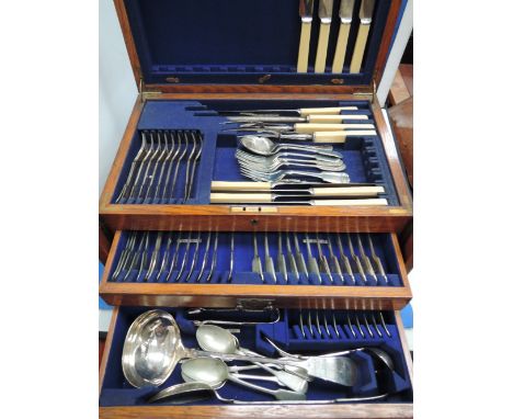 An oak canteen having two drawers and top section containing a selection of flatware including carving set, soup ladle, sugar