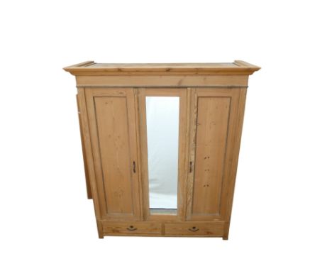 An early 20th century pine armoire - the moulded cornice above three panel doors, one with a mirror, and two drawers, raised 