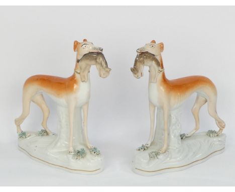 A pair of Staffordshire style greyhounds - standing holding rabbits, 20cm high. (2)