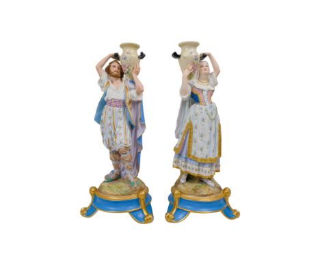 A pair of continental late 19th century lamp bases - modelled as male and female figures in exotic costume and holding urns, 