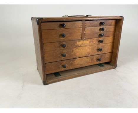A stained oak watch makers eight draw cabinet with an assortment of tools. Stamped M&W. W:51cm x D:22cm x H:34cm