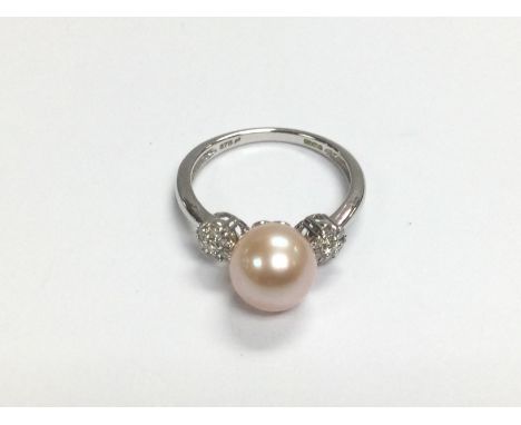 A 9ct white gold ring set with a round peach coloured pearl flanked by daisy cluster of R/C diamonds. Diamonds approx 0.18ct,