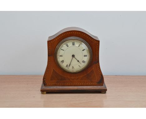 An Edwardian mahogany and boxwood inlaid mantle clock, serpentine shape, enamel dial with Roman Numerals, raised on brass bun