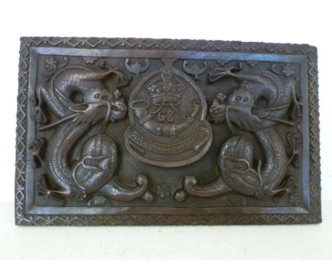 A carved wooden plaque with Durham Light Infantry emblem to centre flanked by Dragons 