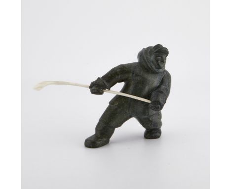 Inuit carved stone figure depicting a man holding a bone instrument or hockey stick. With a sticker from Canadian Eskimo Art 