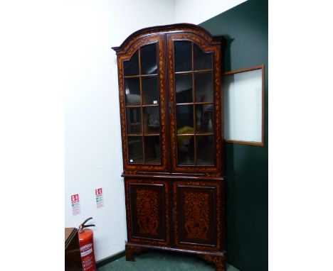 AN ANTIQUE DUTCH MARQUETRY FLOOR STANDING CORNER CUPBOARD WITH SHAPED TOP ABOVE GLAZED DOORS ENCLOSING SHAPED SHELVES AND DRA