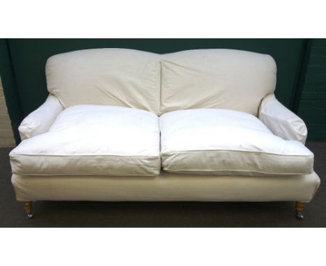 A Howard style three seat sofa, with loose cream upholstery, on turned supports, 225cm wide x 84cm high.