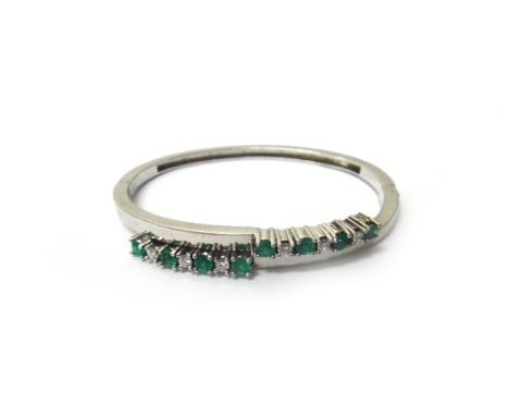 An emerald and diamond set oval hinged bangle, the front mounted with two rows of four circular cut emeralds, alternating wit