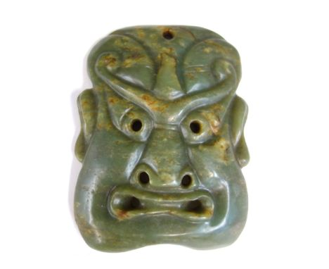 A Chinese jade mask, carved as a grimacing face, with pierced eyes, nostrils and mouth, 15cm.high.