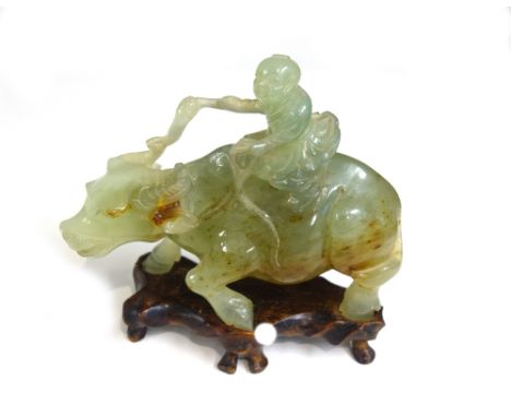 A Chinese celadon jade group of a boy on a water buffalo, 19th/20th  century, the stone with russet inclusions, 18cm. length,