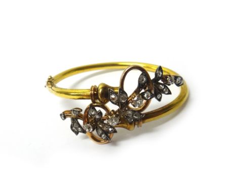A gold and silver set diamond bangle, the front decorated with a foliate spray motif, mounted with cushion shaped and rose cu