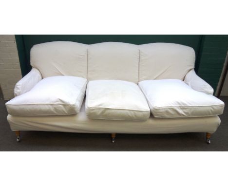 A Howard style three seat sofa, with loose cream upholstery, on turned supports, 180cm wide x 84cm high.