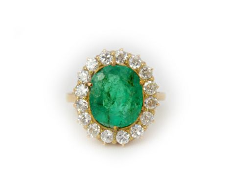 A gold, emerald and diamond cluster ring, claw set with the oval cut emerald at the centre, within a surround of cushion shap