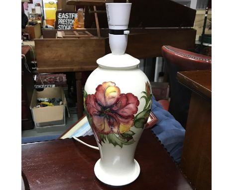 A William Moorcroft table lamp in the Hibiscus pattern against a white background. Has original sticker to the base. In a wor