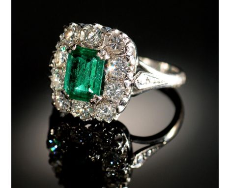 AN EMERALD AND DIAMOND RING&nbsp; the step cut emerald of approx 4 x 6mm in a surround of ten evenly sized round brilliant cu