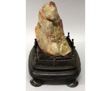 A CHINESE SOAPSTONE BOULDER, together with a fitted wood stand, the stone decorated with figures in a boat near a pagoda, the