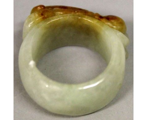 A CHINESE CELADON JADE RING, carved in relief with a resting chilong, the stone with russet inclusions, 1in diameter, the inn