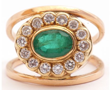 Emerald and diamond cluster ring, a stylised design, the centre with an oval faceted emerald, 8mm x 6mm in rub-over setting w