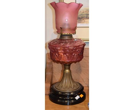 Late 19th/early 20th Century oil lamp having cranberry glass moulded reservoir on circular ceramic base with pink glass shade
