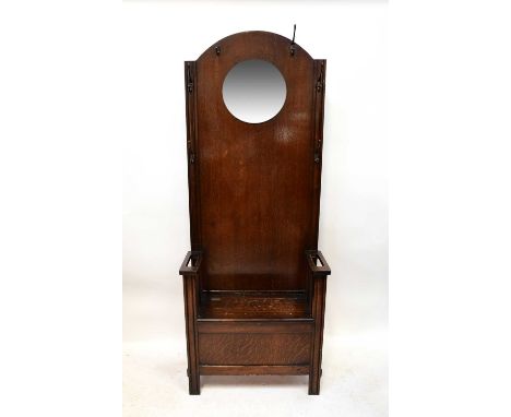 An early 20th century oak hall bench, the arched upper section fitted with circular mirror surrounded by coat hooks, above a 