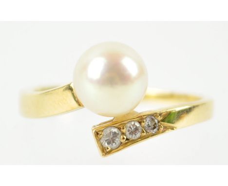 A yellow metal dress ring of crossover design set with a 7.0mm cultured pearl and three graduated round brilliant cut diamond