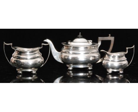 A George V hallmarked silver three piece tea service comprising teapot, sugar bowl and cream jug, each of cushioned rectangul