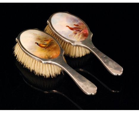 A pair of dressing table hairbrushes each set with a Royal Worcester oval panel decorated by James Stinton, the first decorat