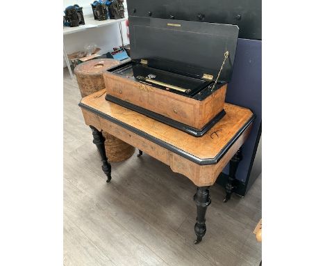 A cylinder musical box and table, figured walnut with crossbanding, ebonised turned supports to castors, ormolu mounts. Thoug