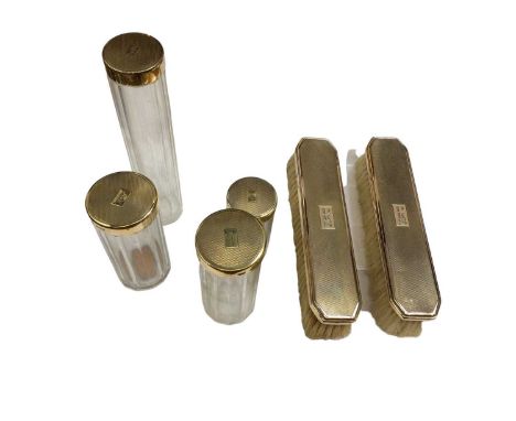 Silver gilt toiletry set, including four jars and two brushes, London 1934, each with engine turned decoration and initials '