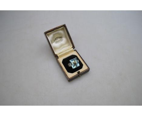 A single stone Art Deco ring set with rectangular step cut aquamarine having three diamonds on each shoulder, in ornate baske