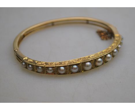 A Victorian graduated hinged bangle set with half-pearls having engraved sides, and fitted with safety chain, yellow gold set