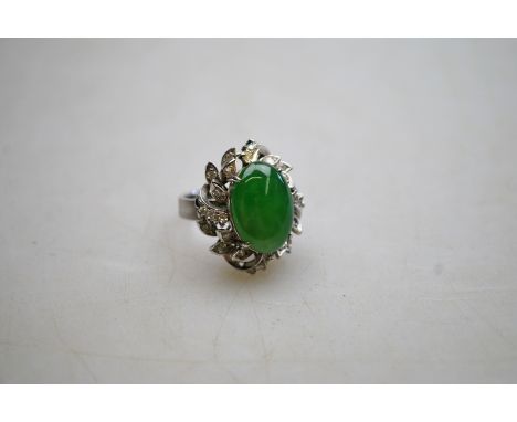 A cabochon green stone, probably jade, and diamond cluster cocktail ring, white metal set, stamped 18k Condition Report About