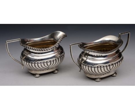 AN OVAL SHAPED SILVER CREAM JUG with fluted lower body, gadrooned edge and standing on four bun feet, with matching sugar bas