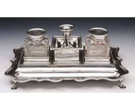 A LARGE EDWARDIAN SILVER DESK STAND, rectangular with shaped sides, two silver mounted square shaped ink bottles and candlest