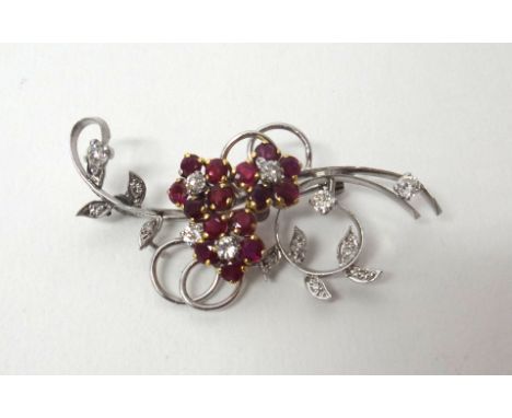 A diamond and ruby set brooch, designed as a floral and foliate spray, each of the three flowerheads centred by a circular cu