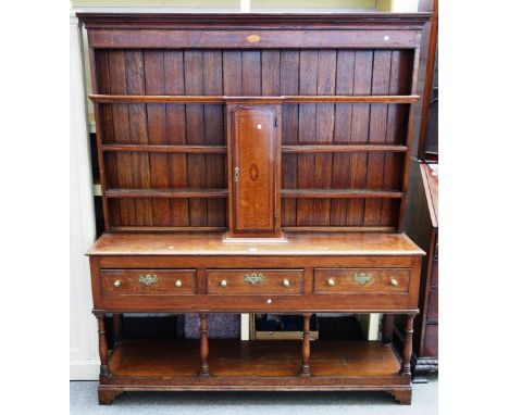 An inlaid George III oak dresser, the enclosed three tier plate rack with central spice cupboard over three frieze drawers on