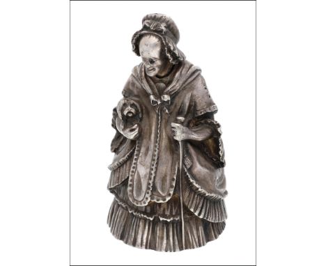 A white metal table bell, modelled as an elderly Victorian lady, wearing a crinoline dress, shawl and bonnet, and carrying a 