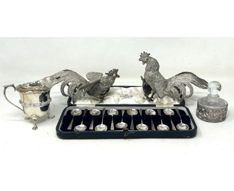 A set of twelve silver coffee spoons, a silver cream jug, a pair of silver plated fighting cockerels, and a silver cased glas