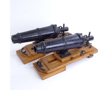 A pair of cast-iron barrelled model cannons on stained oak stands, overall barrel length 28cm, base length 35cm, probably mid