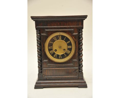 An oak mantel clock, the circular dial with Roman numerals flanked by barley twist supports