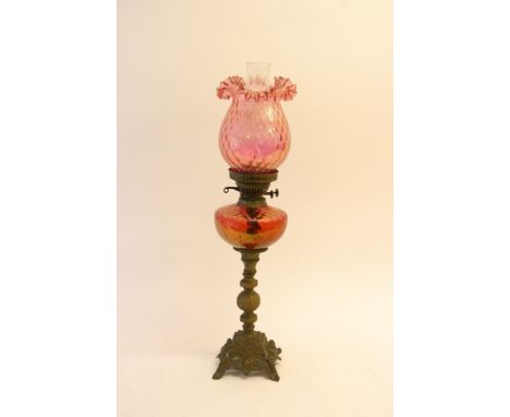A gilt metal oil lamp with cranberry glass shade and reservoir.