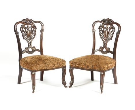 A pair of Victorian fireplace chairsMahoganyWith pierced backs carved with vegetal scroll motifsFront legs with castors Engli