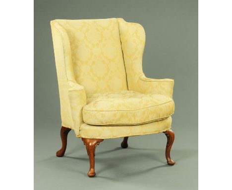 A Queen Anne style wing armchair, raised on walnut cabriole legs terminating in pad feet, upholstered in beige and gold folia