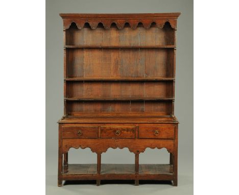 An antique oak dresser with Delft rack, with boarded back and fitted with three frieze drawers above an open potboard and rai