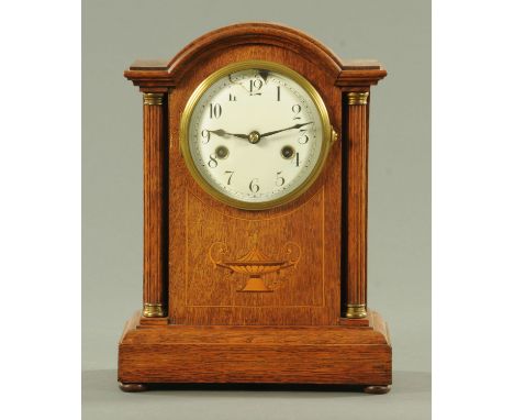 An Edwardian inlaid oak mantle clock, with two-train striking movement, flanked by columns with brass capitals and raised on 