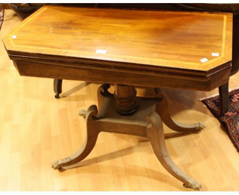 A Regency mahogany card table, crossbanded top enclosing a baize lined playing surface, ring turned column, sabre legs, brass