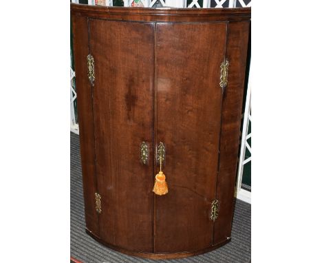 A George III mahogany bow front corner cupboard, enclosing four shelves with decorative brass hinges and escutcheons (with ke