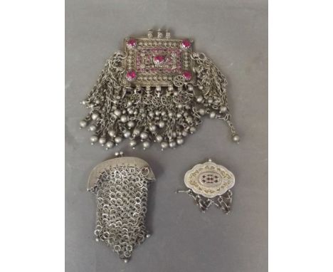 A Turkmeni silver metal pendant set with pink paste stones, a silver metal chain link purse, and another pendant with gilt wa