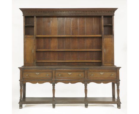 An oak and inlaid dresser, with a moulded cornice and Vitruvian scroll frieze over three shelves, flanked with cupboards belo