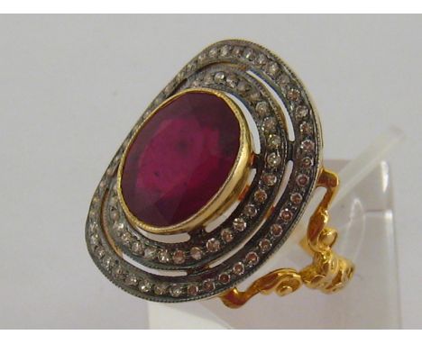 A ruby and diamond dress ring, the central oval cut stone 12.3 x 9.9mm, in a double surround of small brilliants, to an ornat